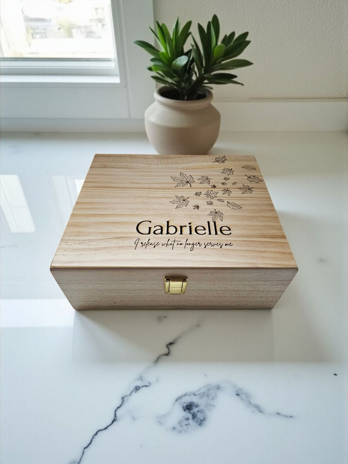 Newfashioned Relics personalized wooden keepsake box with engraved name and leaf design on a white marble surface.